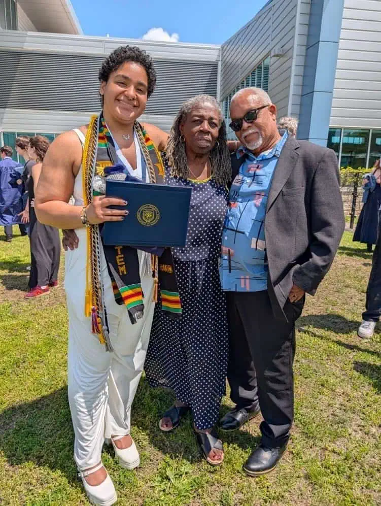 Anika in graduation clothes with their grandmother Lois, who has long gray locs, and her husband Tony, wearing sunglasses. Both drove from Florida.