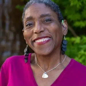 Roxy Manning smiling, wearing a magenta top, in front of green leaves
